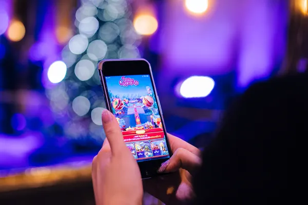 A young woman relaxing with her phone while dynamic casino elements float around her, illustrating the smooth mobile experience offered by the JAYA app.